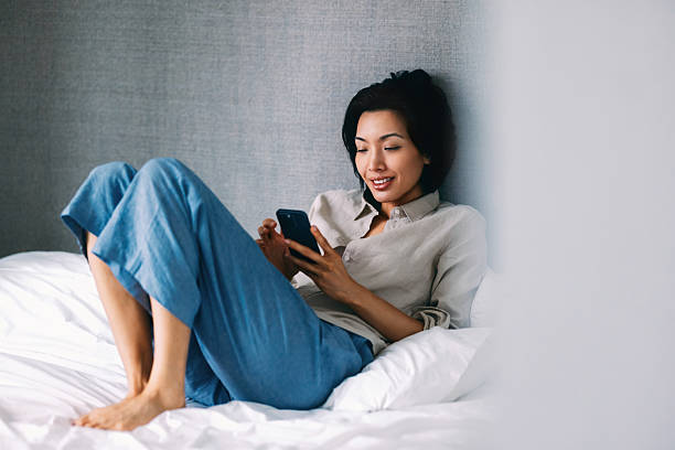 istock Woman Relaxing on Bed While Using Smartphone in a Modern Room 2219204252