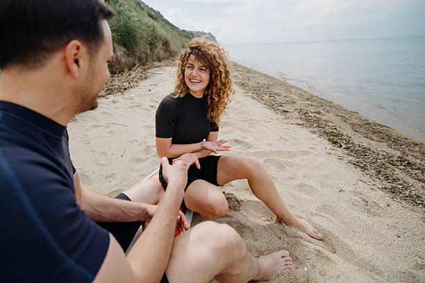 istock Couple relaxing on a surfboard at the beach and chatting 2219205566