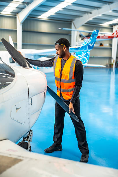 Aircraft maintenance engineer wearing a high-visibility vest, inspecting the propeller of a small airplane inside an aircraft hangar