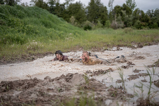 Two enthusiastic individuals take on the challenge of a muddy obstacle race in the outdoors, showcasing determination, physical effort, and enjoyment in a natural and competitive environment.