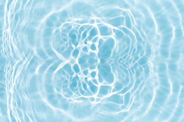 Blue water with ripples on the surface. Defocus blurred transparent blue colored clear calm water surface texture with splashes and bubbles. Water waves with shining pattern texture background.