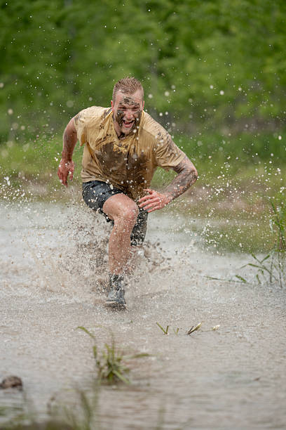 Athletic man splashing through muddy water, showing determination and energy during a challenging mud run event outdoors.