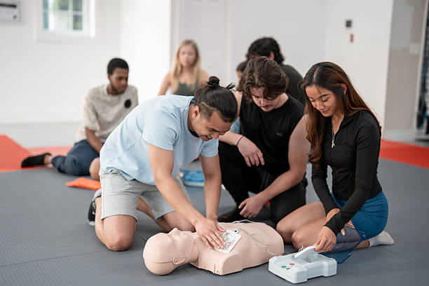 Group Learning CPR Techniques Using Practice Dummies in a Training Class A diverse group of individuals attend a first aid and CPR training class, practicing lifesaving techniques on dummies and using AED equipment under supervised guidance. cpr stock pictures, royalty-free photos & images