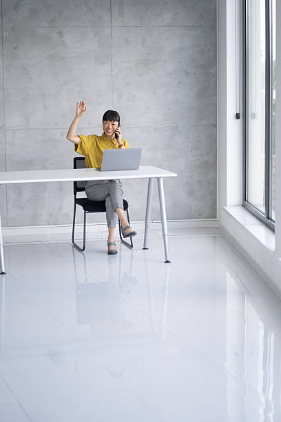 istock Cheerful Woman Wave While Speaking on Phone at Desk 2219227628
