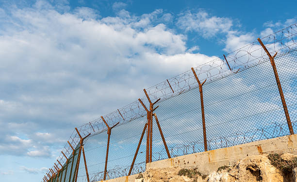 istock Security fence with barbed wire against a blue cloudy sky. Security border forbidden access 2219228286
