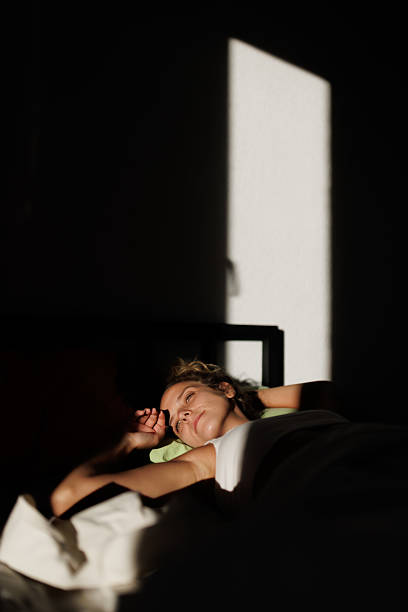 istock Woman relaxing on a bed with soft sunlight streaming through a window in a serene bedroom setting 2219229102