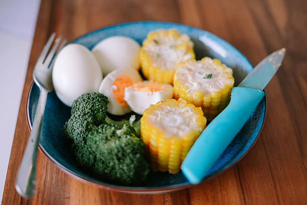 Healthy food plate with boiled eggs, broccoli and corn cobs. Balanced meal on wooden table