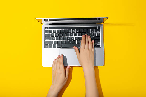 istock Female hands and laptop on yellow background 2219250138