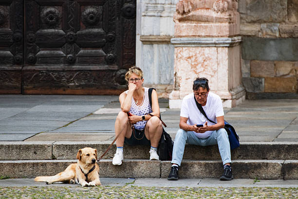 Parma, Italy June 3, 2025: A couple and their dog relax on stone steps outside a historic building in an Italian city.