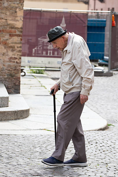 Parma, Italy June 3, 2025: Senior gentleman in casual attire taking a stroll outdoors with a historic building in background.