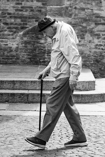 Parma, Italy June 3, 2025: An elderly man walks with a cane on a cobblestone street captured in monochrome.