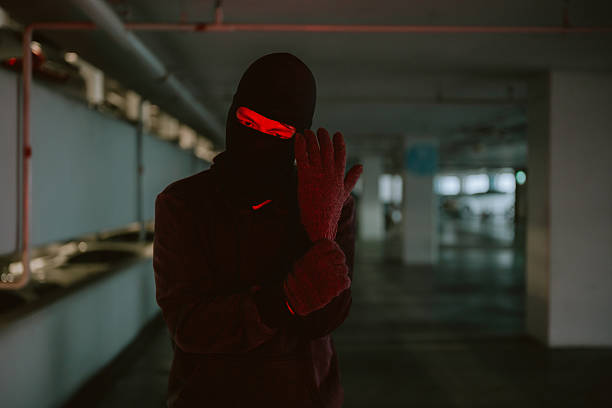 Mysterious figure dressed in black stands ready for action in a dimly lit parking garage at night
