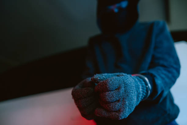 An individual sits on a surface with their hands in front, wearing gloves and handcuffs. The background is dark with colorful lighting, creating a tense atmosphere.