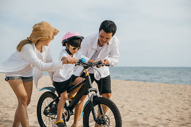 istock Sunset happiness on sandy beach, cheerful family engages in road trip teaching and learning bicycle riding. Safety laughter and joy of family bonds make this perfect summer vacation concept. 2219251964