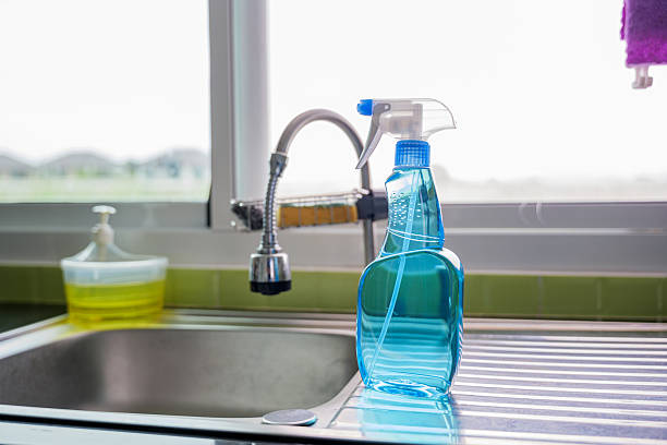 istock Blue cleaning spray bottle placed on silver kitchen sink with a faucet in background. Represents modern cleaning tools and hygiene in kitchen setting. Glass spray bottle emphasizes cleaning 2219252193