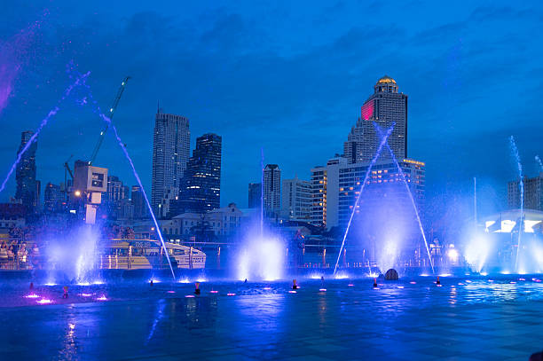 Bangkok, Thailand - July 25, 2024: An awe-inspiring view of the green-illuminated fountain show at night in front of Icon Siam Mall, featuring layers of synchronized water jets and ambient city lighting. Visitors are seen enjoying the immersive visual experience set along the river, highlighting Bangkok's status as a top entertainment and shopping hub in Southeast Asia