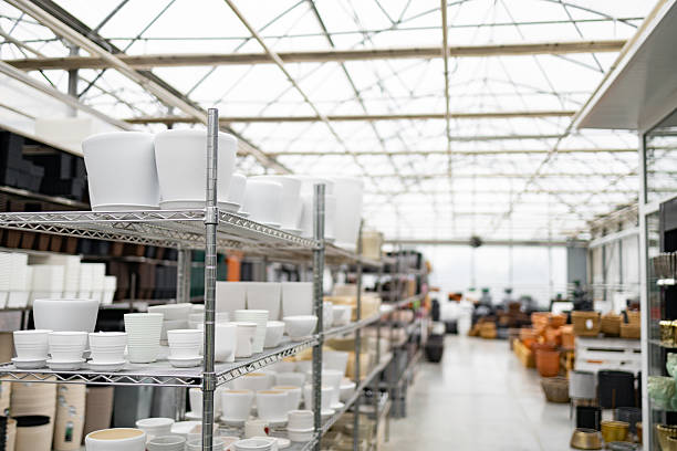 A shop selling a variety of white flower pots on display, arranged on metal shelving under a bright glass ceiling, ready for plants.