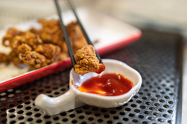 Close-up of a crispy deep fried spicy chicken piece being dipped into chili sauce using chopsticks at a local eatery.