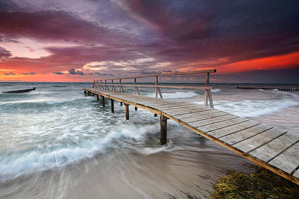 stormy sunset at the beach, wooden jetty on sea
