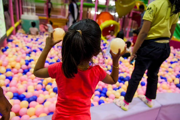A young child plays with white balls in a colorful ball pit at a lively indoor recreation area.