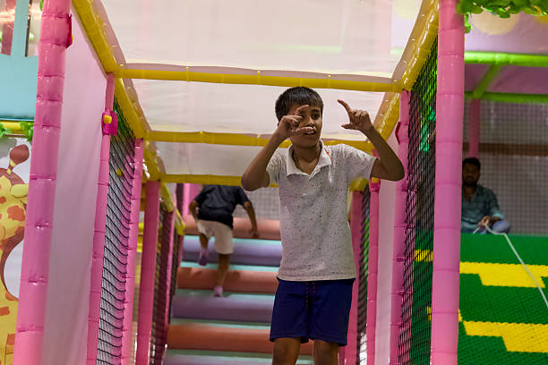 A happy child poses with fingers shaped like a frame in an indoor play area while others enjoy climbing and jumping.