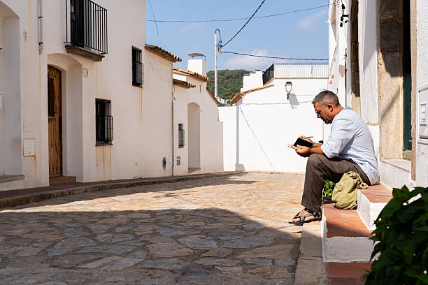istock Mature writer working on notebook while seated on whitewashed Mediterranean village doorstep, capturing peaceful moment 2219266493