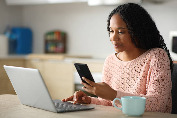 istock Serious black woman using cell phone and laptop in a kitchen 2219272936
