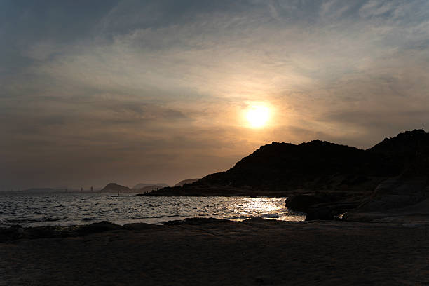 Golden sunset casting a warm glow over a rugged coastline, with calm waves gently reflecting the vibrant colors of the evening sky