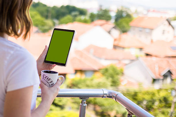 Tablet with green screen held by woman in casual setting.