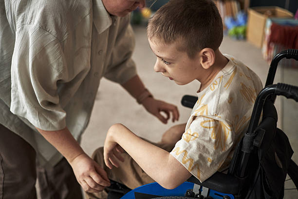 istock Assisting Young Boy with Disability in Bright Room 2219280800