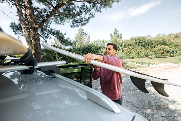 istock Man loading surfboard onto car roof rack 2219285356