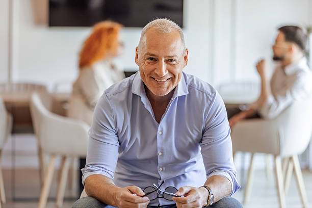 istock Smiling Man Seated in Office Environment with Colleagues in Background 2219285611