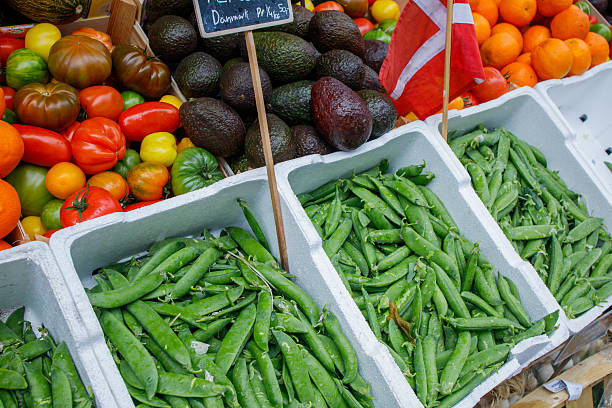 Different vegetables well organized and presented on food market in Denmark. Fresh green peas, tomatoes, avocado in boxes close up. Danish flag as a symbol of local products.