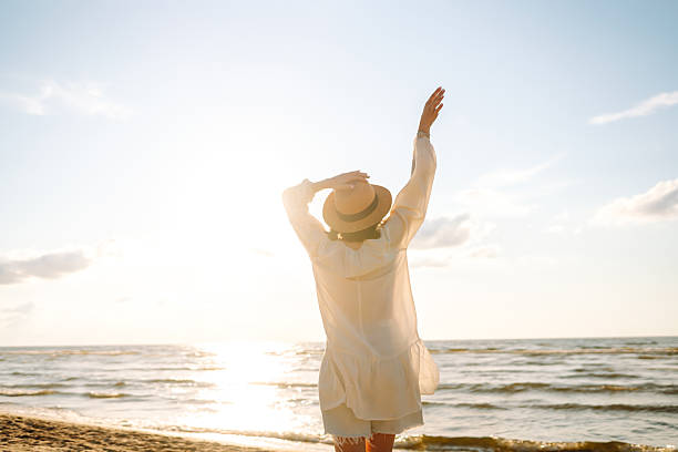 istock Smiling woman wearing hat and sunglasses walking on sunny beach. 2219288421