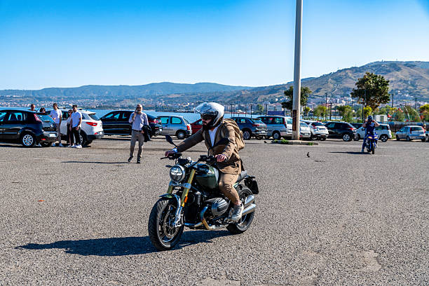 Reggio Calabria - Kalabrien - 05-18-2025: Motorcyclist in suit riding through parking lot during the Distinguished Gentlemans Ride in Reggio Calabria with cars and hills behind.
