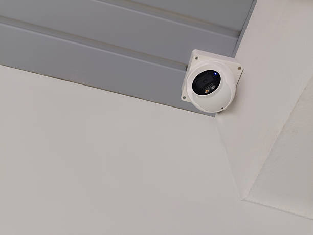 istock Black and white CCTV camera mounted on a grey roof and white wall background, object, technology, care, decor, copy space 2219295727