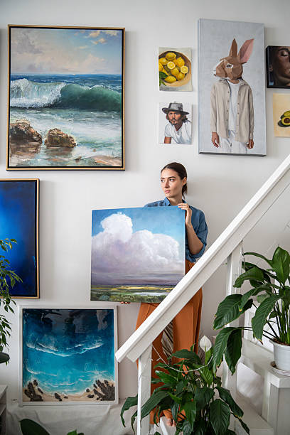 istock Serious pensive woman with canvas makes creative art composition from paintings on studio wall. 2219297958