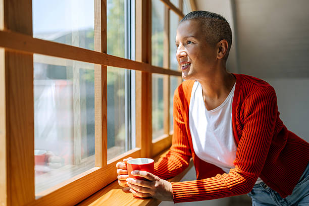 istock Woman enjoying quiet moment at home looking through window with coffee cup 2219298667