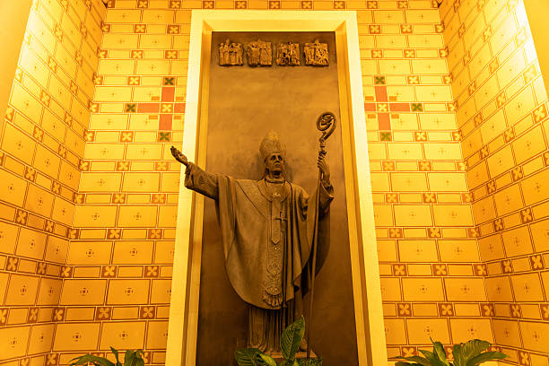 Reggio Calabria - Kalabrien - 05-22-2025: Bronze statue of a bishop in ceremonial robes and mitre, holding a crozier and extending one arm, set in a decorated alcove with patterned wall