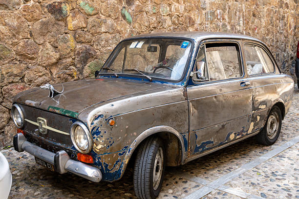 Scilla - Kalabrien - 05-27-2025: Weathered Fiat with visible rust spots parked on cobblestone street in Scilla, Calabria, next to a textured old stone wall