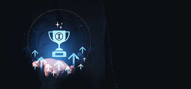 istock Digital trophy icon hovering above a hand with glowing arrows and sparkles representing success and achievement on a dark background with futuristic style. 2219300218