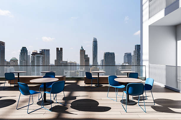 istock Rooftop terrace with modern blue chair and table design overlooking a city skyline under clear blue sky with bright sunlight and shadows cast on floor. 3D Rendering 2219300874