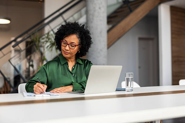 istock Mature Businesswoman Working at a Laptop While Writing in a Notebook 2219301520