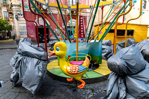 Catania, Sizilien - Italy - 04-15-2025: Colorful childrens carousel in Catania with a duck-shaped seat surrounded by covered elements and set on a paved urban square near buildings.