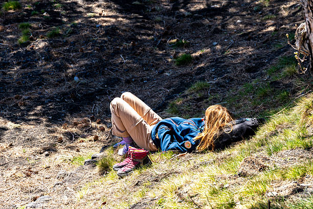 Catania, Sizilien - Italy - 04-22-2025: Woman lies on grassy slope in the shade of a forest near Etna base camp, shoes removed, resting peacefully in natural surroundings.