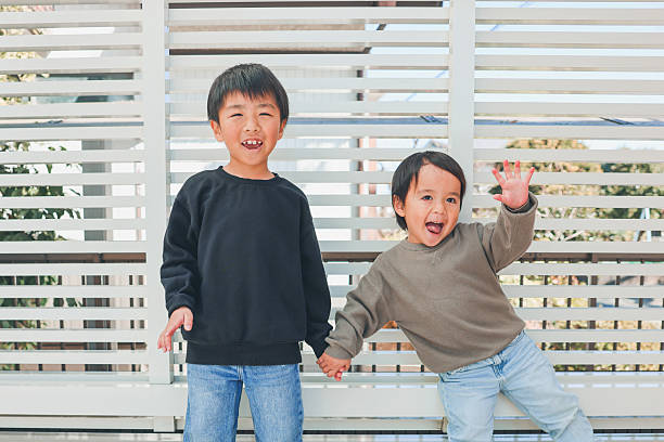 Asian elementary school girl smiling and looking at the camera and making a peace sign in front of a white background