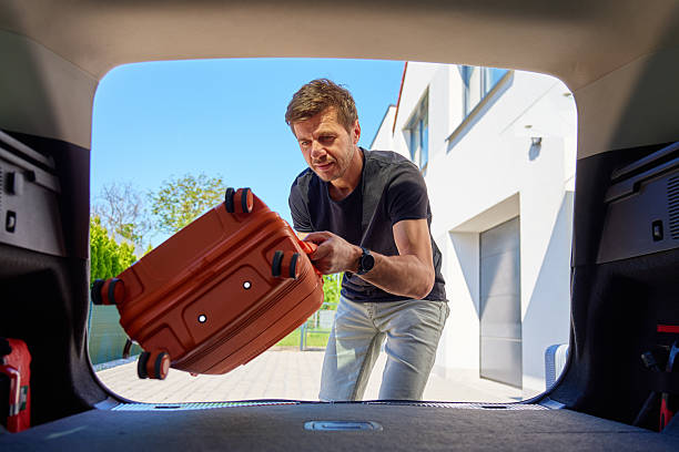 istock Man loading suitcase into car trunk before travel departure 2219309081