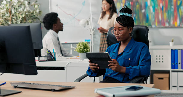 istock In a corporate office, co-workers collaborate on a new project at the blackboard, drawing a graph, while a woman in a blue shirt, uninterested, holds a tablet and plays games instead of helping. 2219311933
