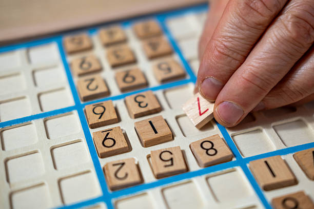 close-up hands carefully placing number into Sudoku puzzle, elderly person deeply engrossed in solving challenging puzzle, mental stimulation and enjoyment classic game provides, brain health