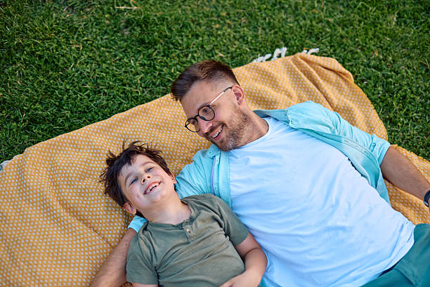 istock Father and son lying on blanket in park looking at each other 2219324417